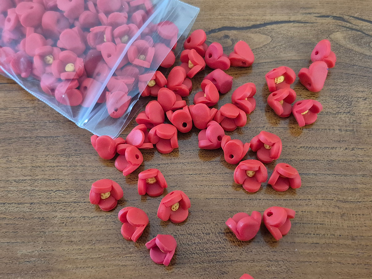 Pink flower-shaped beads with yellow centers scattered on a table beside clear packets