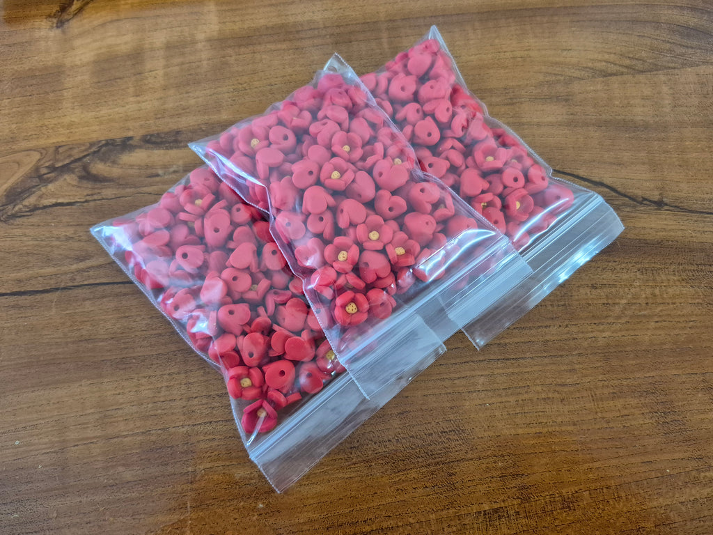 Set of three clear plastic packets filled with pink flower-shaped beads with yellow centers