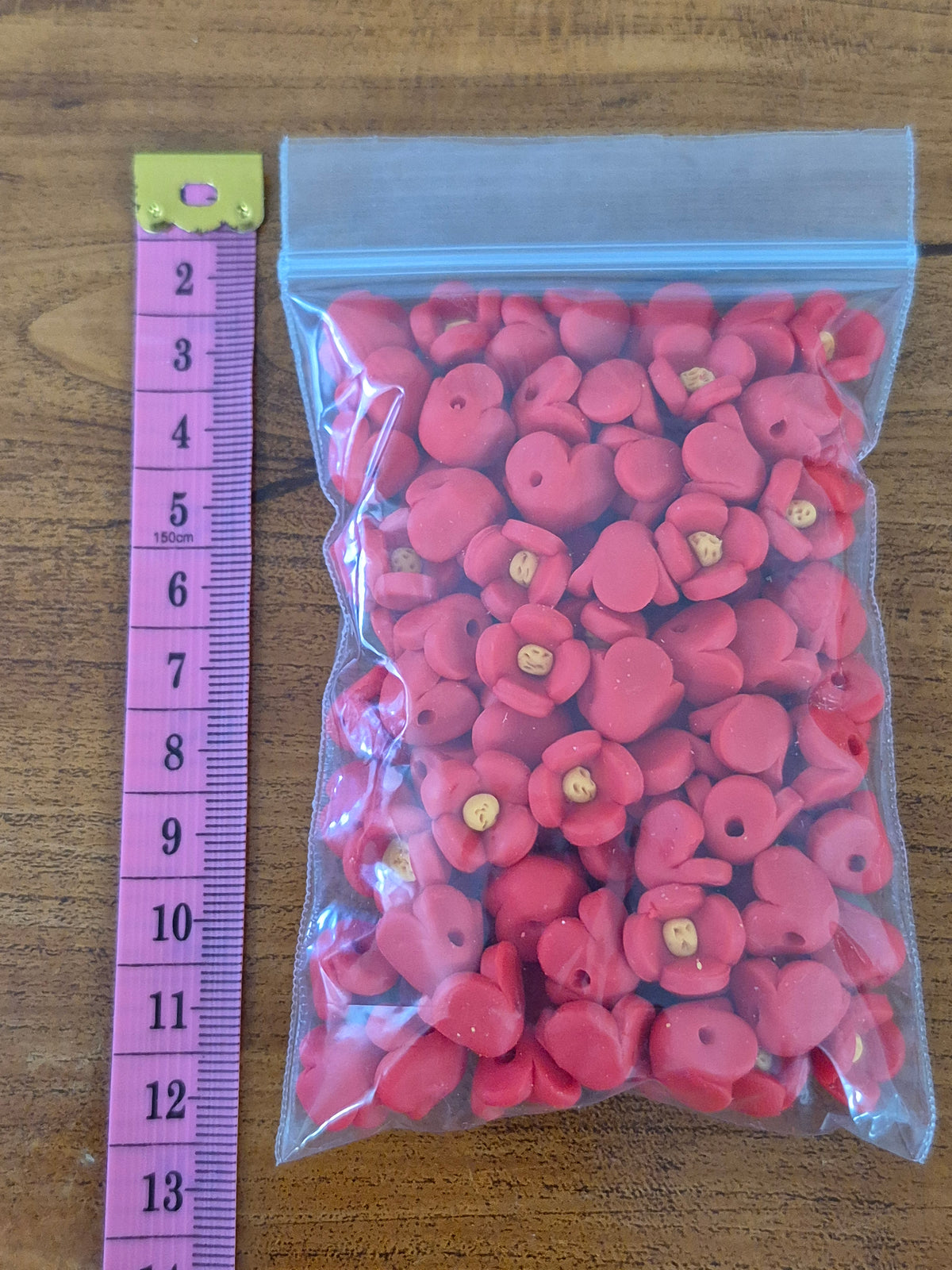 Plastic packet of pink flower-shaped beads with yellow centers beside a height ruler