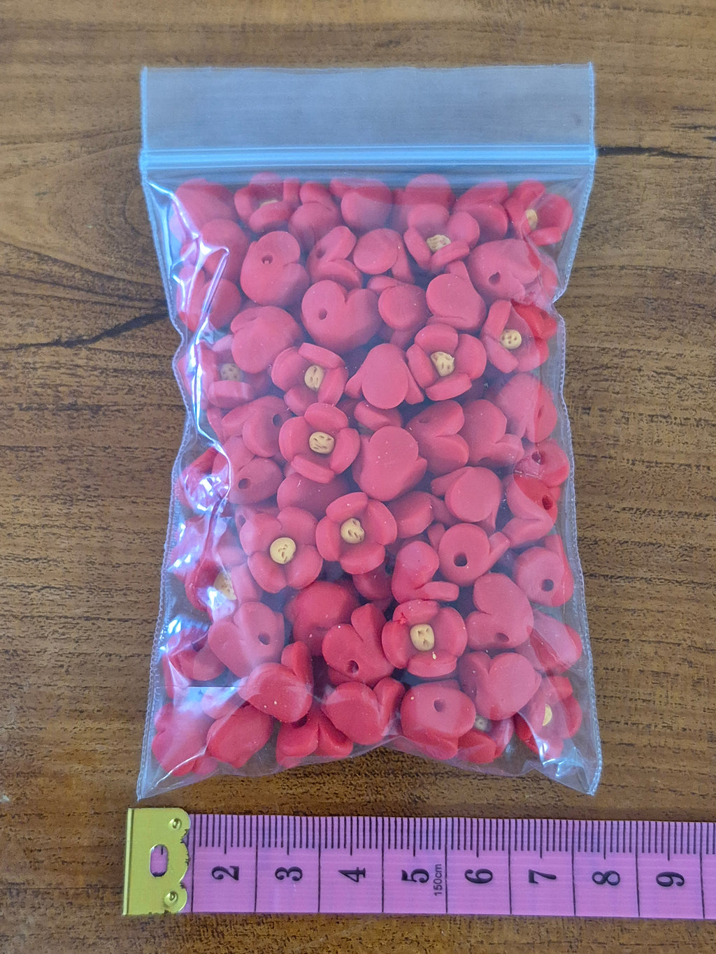 Plastic bag of pink flower-shaped beads with small yellow centers, with measuring scale