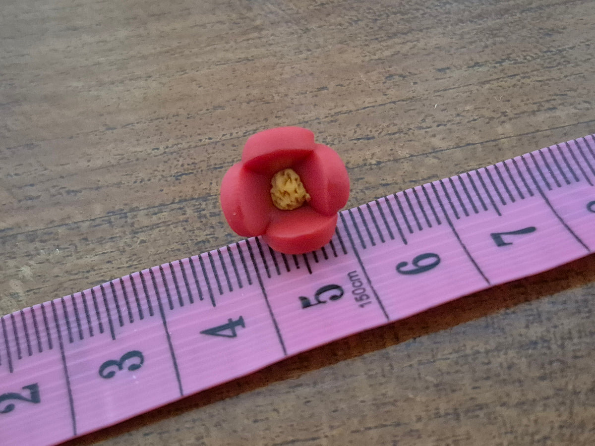 Pink flower-shaped bead with yellow center, shown beside a measuring ruler