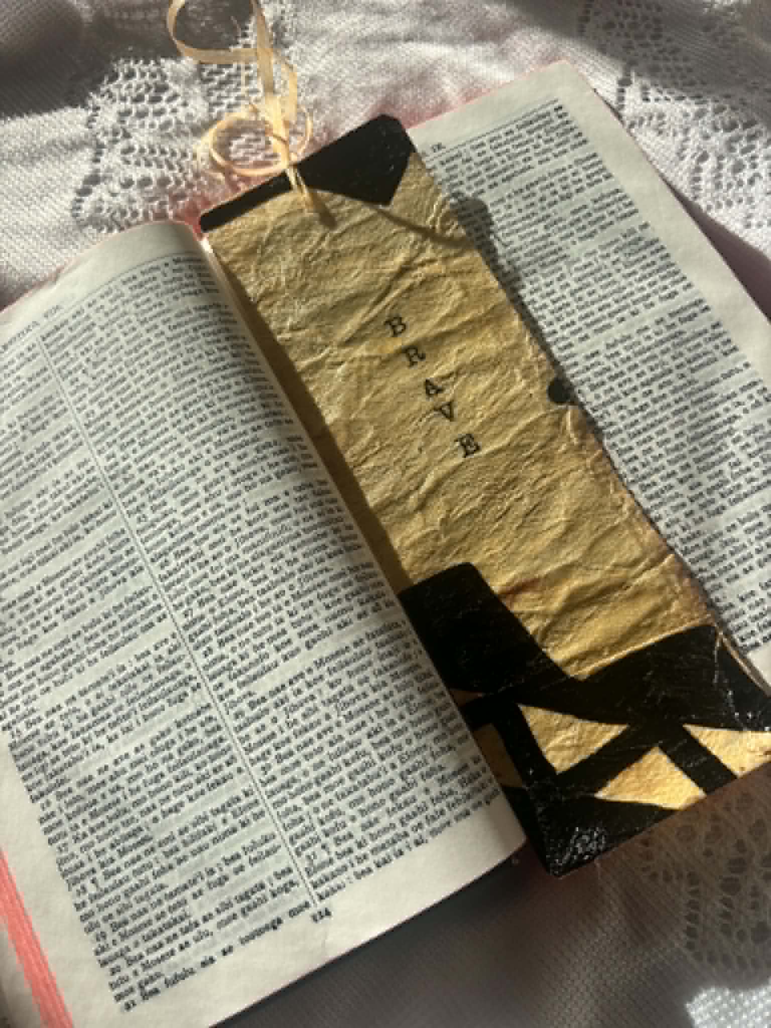 Gold fabric bookmark with black cross symbol and hanging cord on book