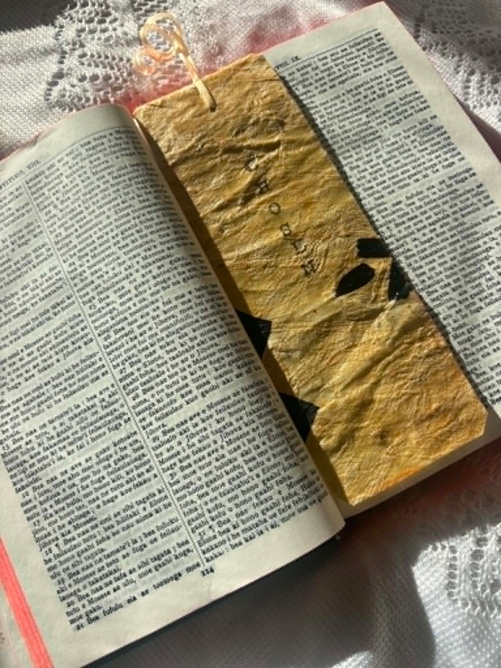 Gold bookmark with black letter shapes and dangling tassel, partially visible in open book