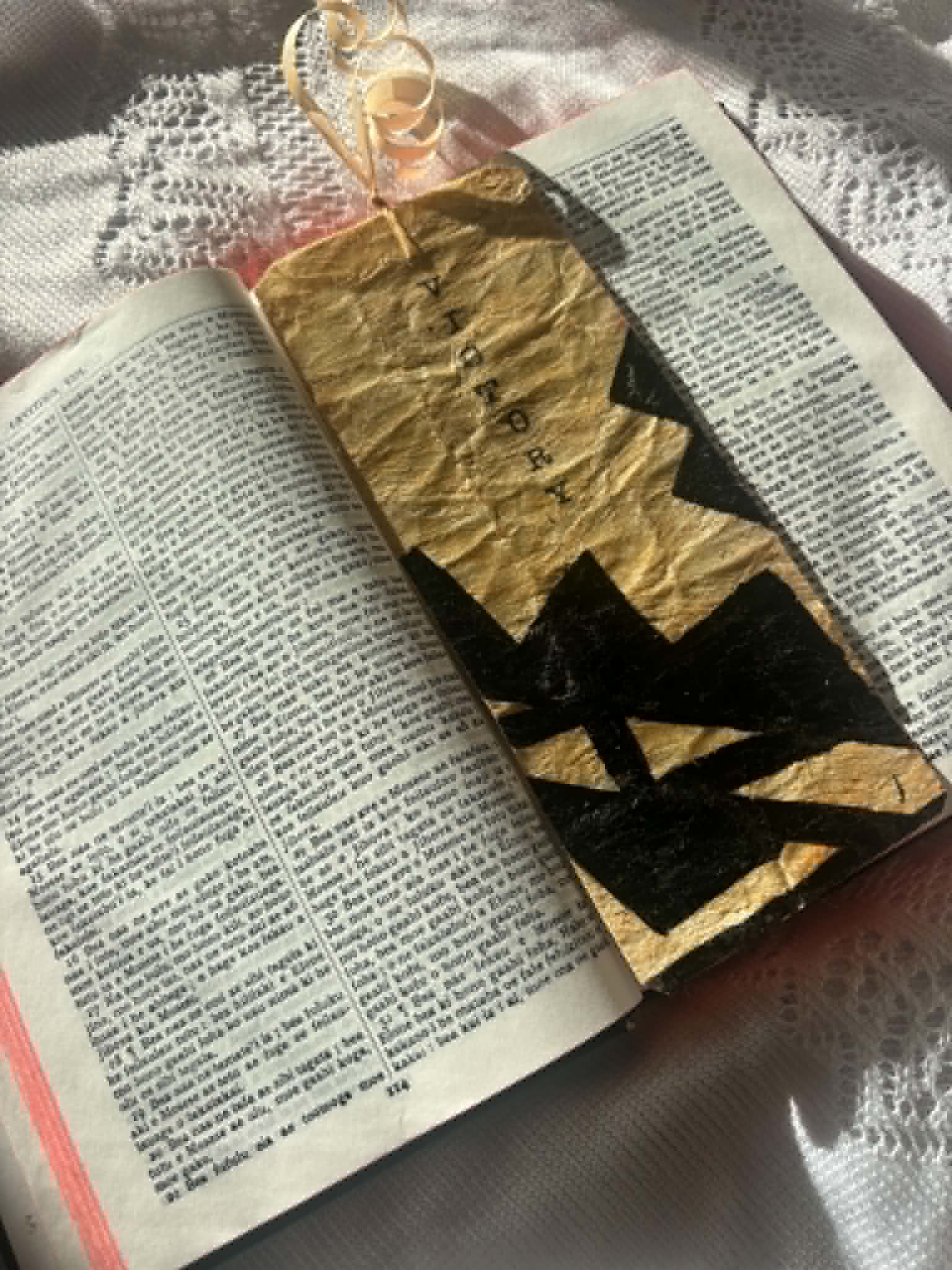 Gold bookmark with black letter silhouette and tassel loop, on an open book