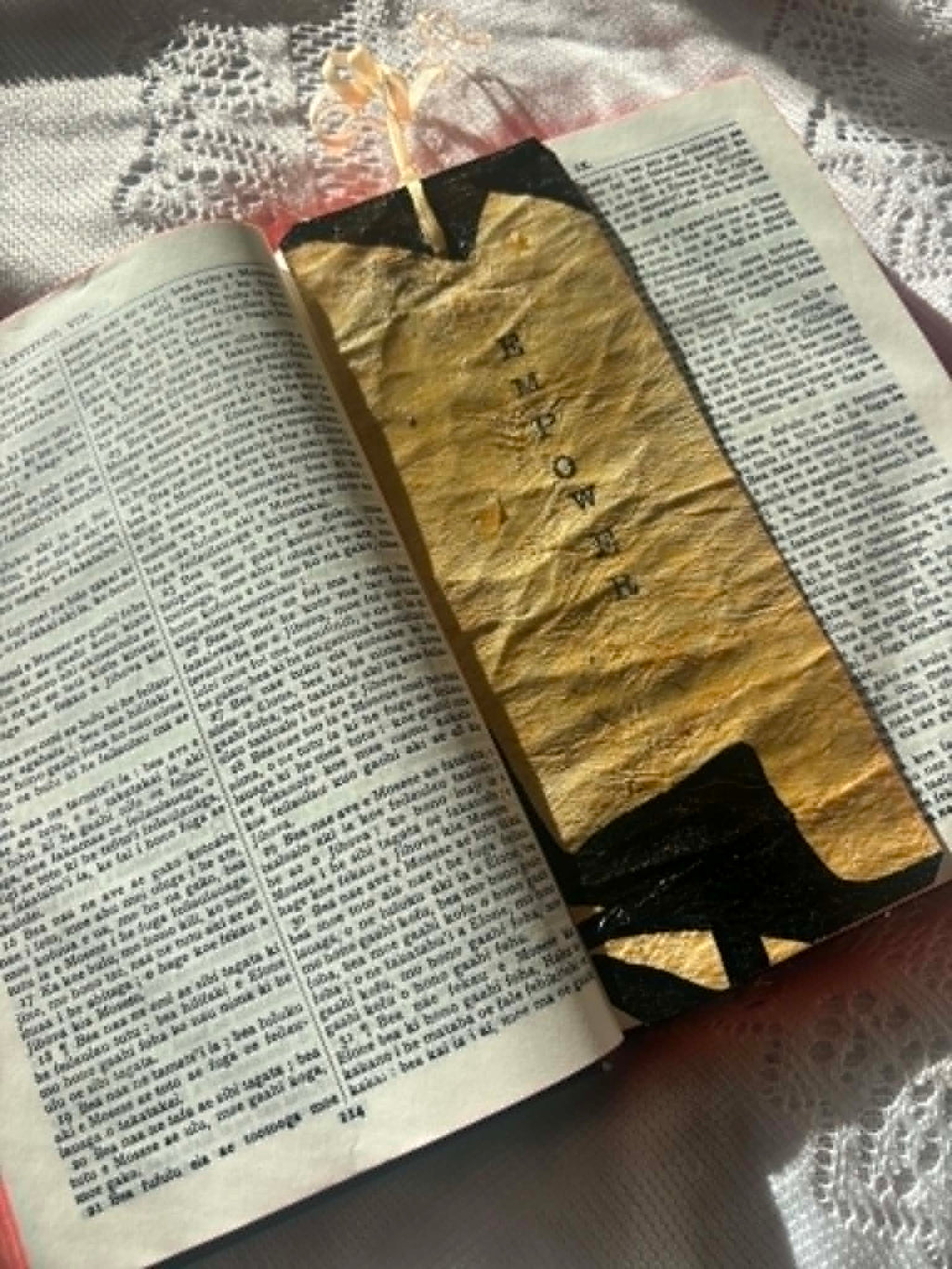 Gold bookmark with black letter shapes and tassel, shown across open pages