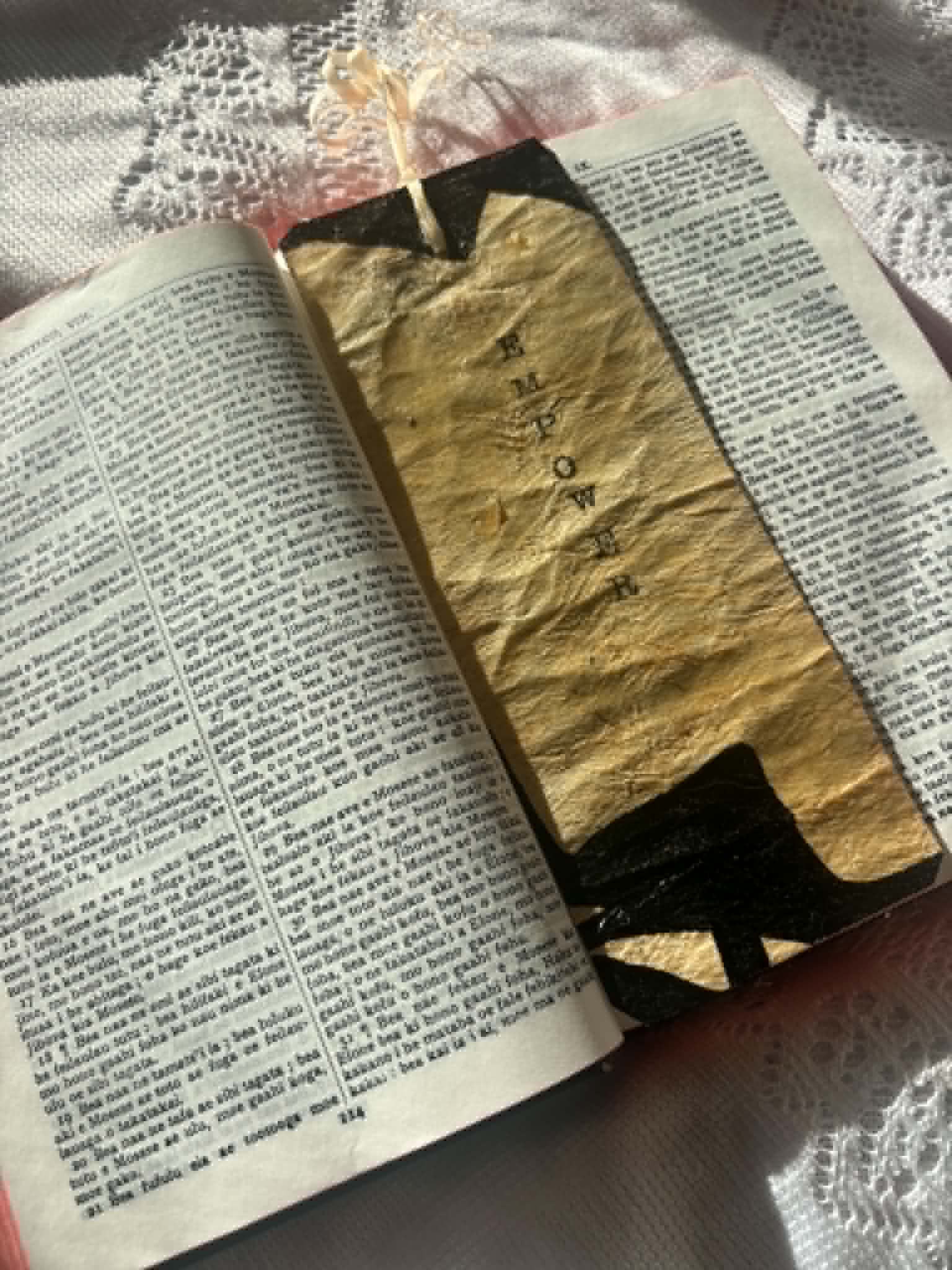 Gold bookmark with black letter shapes and tassel, shown across open pages