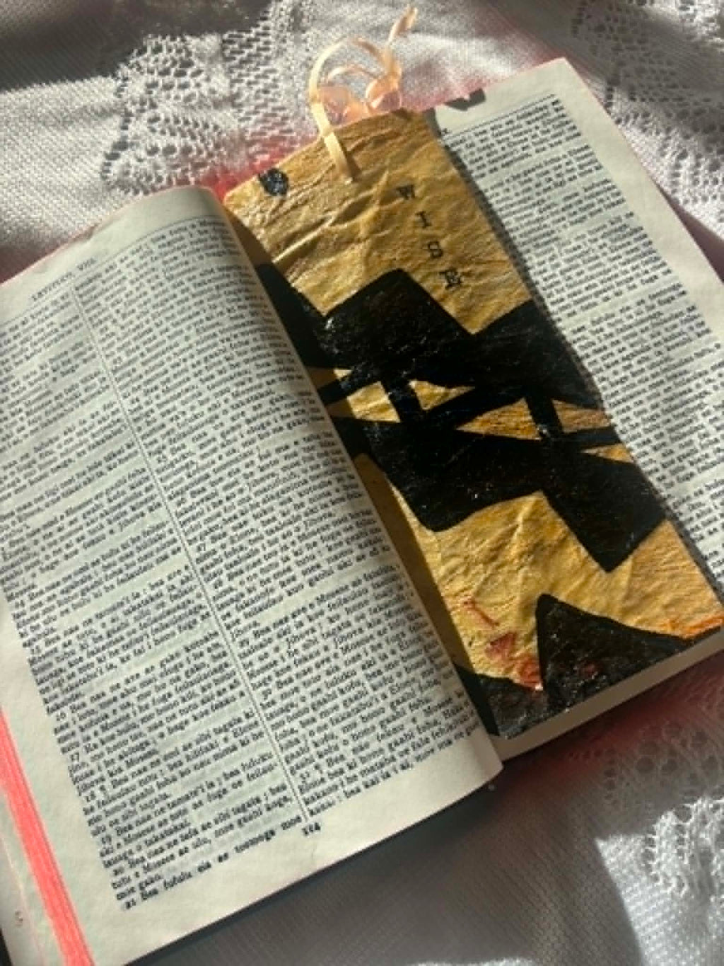 Gold fabric bookmark with black cross design and tied cord on open page
