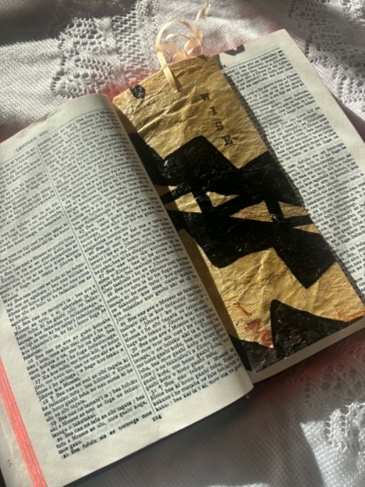 Gold fabric bookmark with black cross design and tied cord on open page