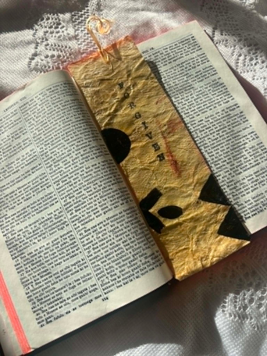 Gold fabric bookmark with black cross symbol and tied cord on open book