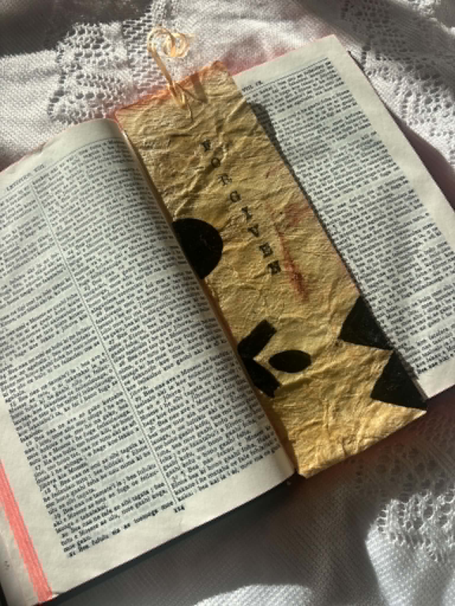 Gold fabric bookmark with black cross symbol and tied cord on open book