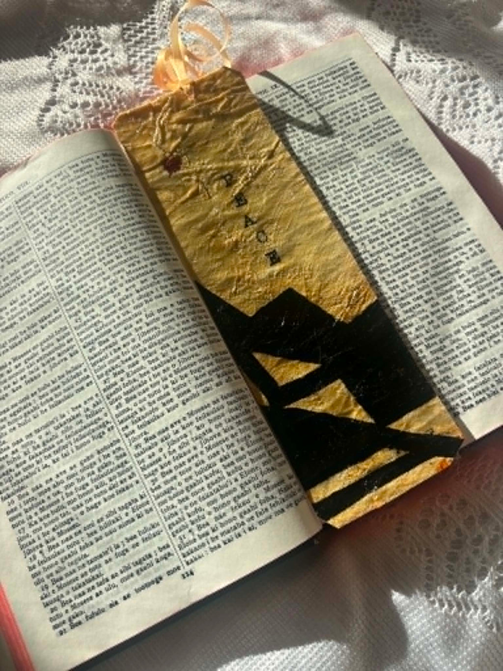 Gold bookmark with black letter silhouette and tassel, positioned in an open book