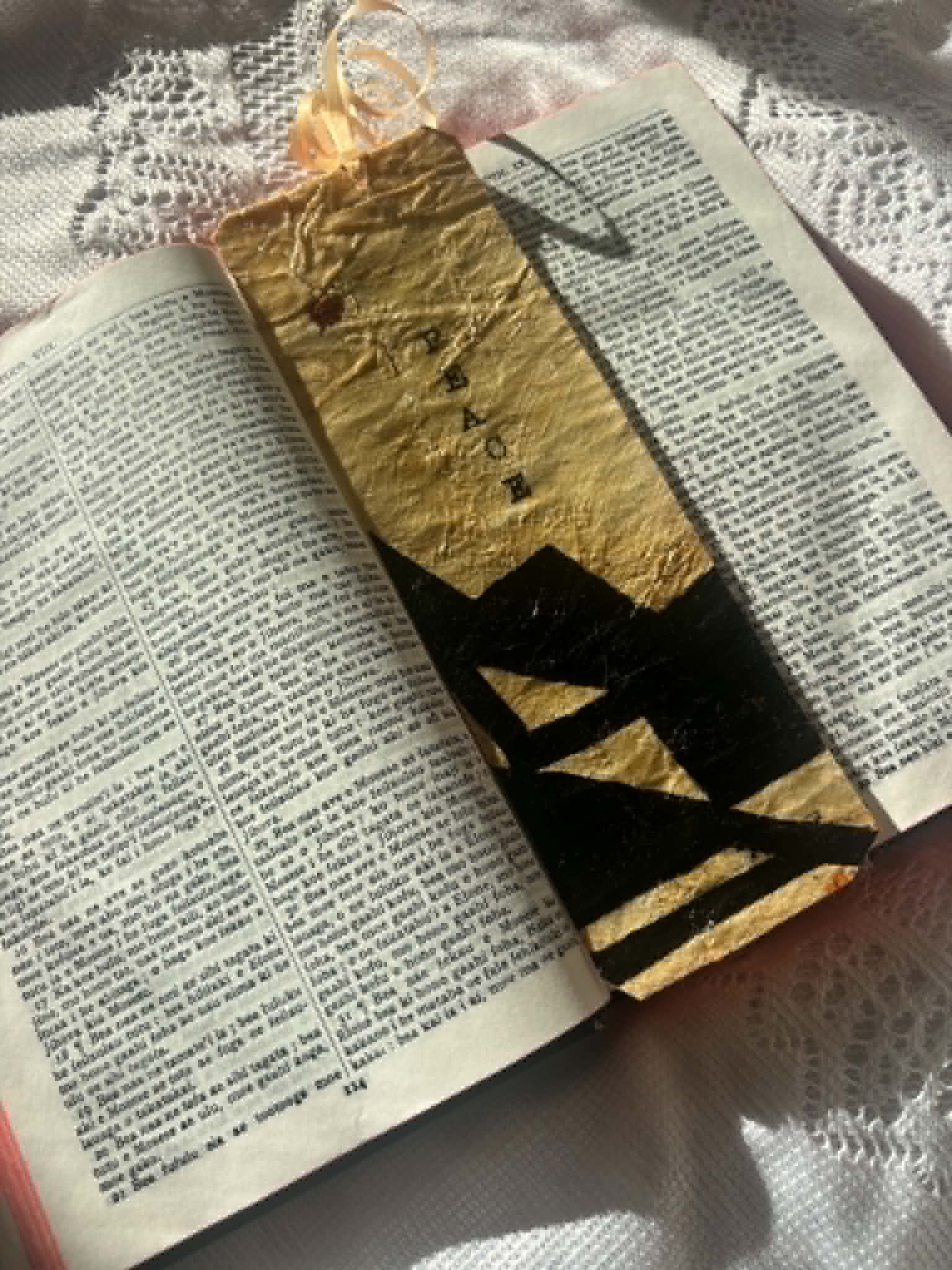 Gold bookmark with black letter silhouette and tassel, positioned in an open book