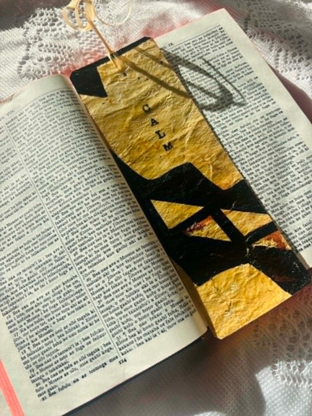 Gold bookmark with bold black letter shapes and tassel, resting across open pages