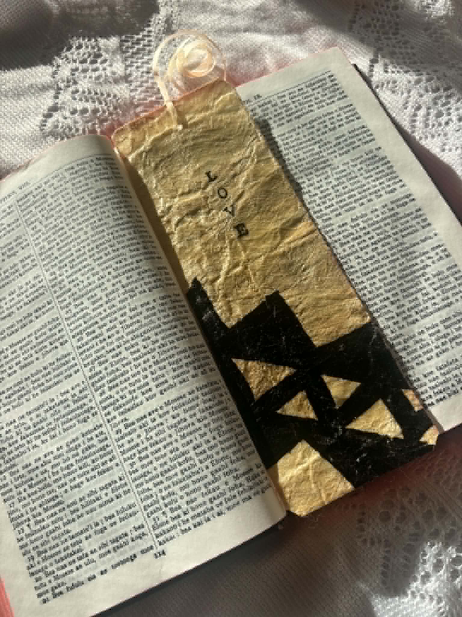Gold fabric bookmark with black cross design and cord tie on open book