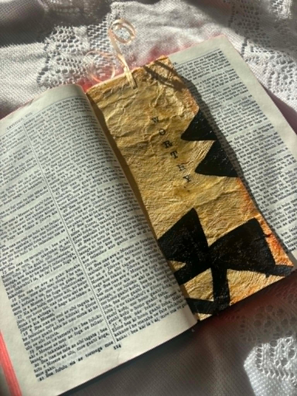 Gold foil bookmark with black cross cutout and ribbon tassel on open page