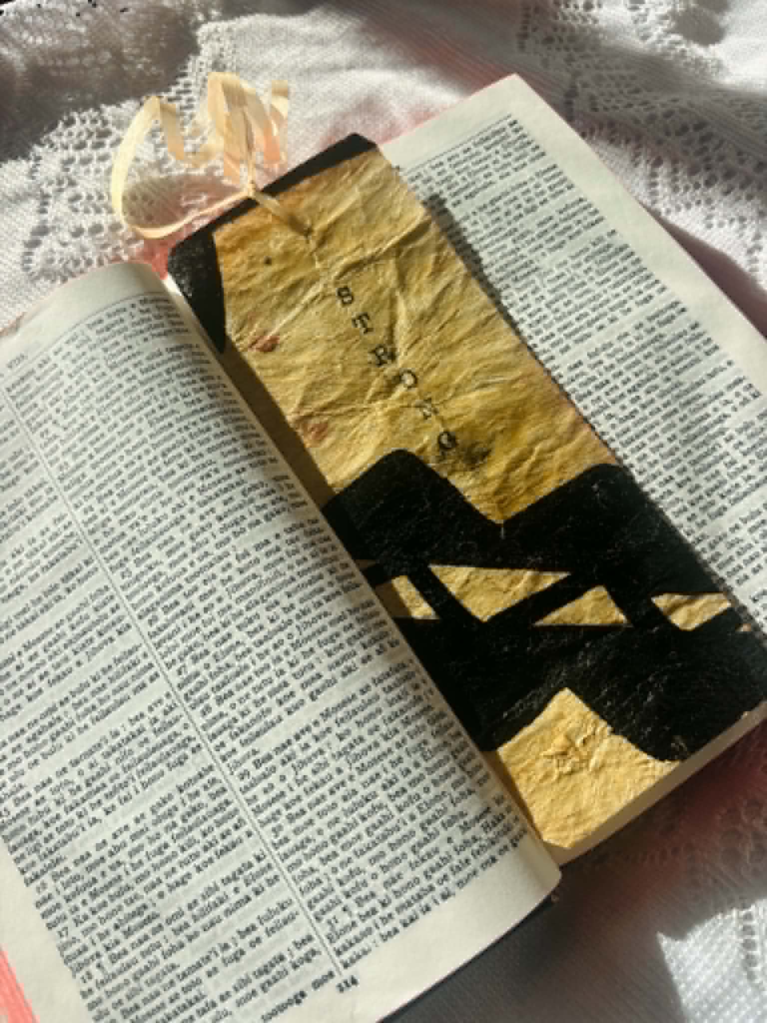 Gold bookmark with black letter silhouette and top tassel, shown on open text pages