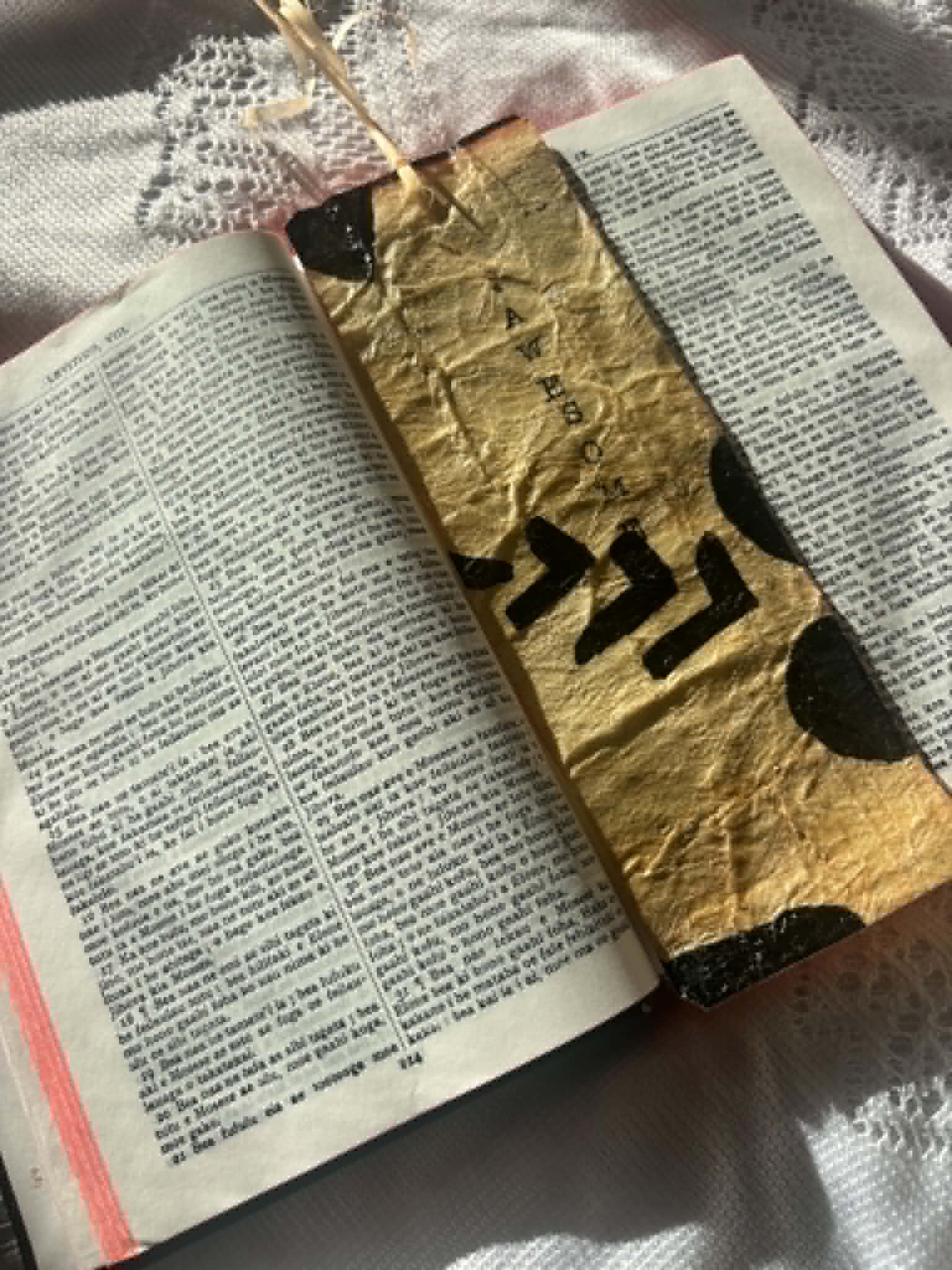 Gold bookmark with black letter silhouette and tassel, resting in an open book
