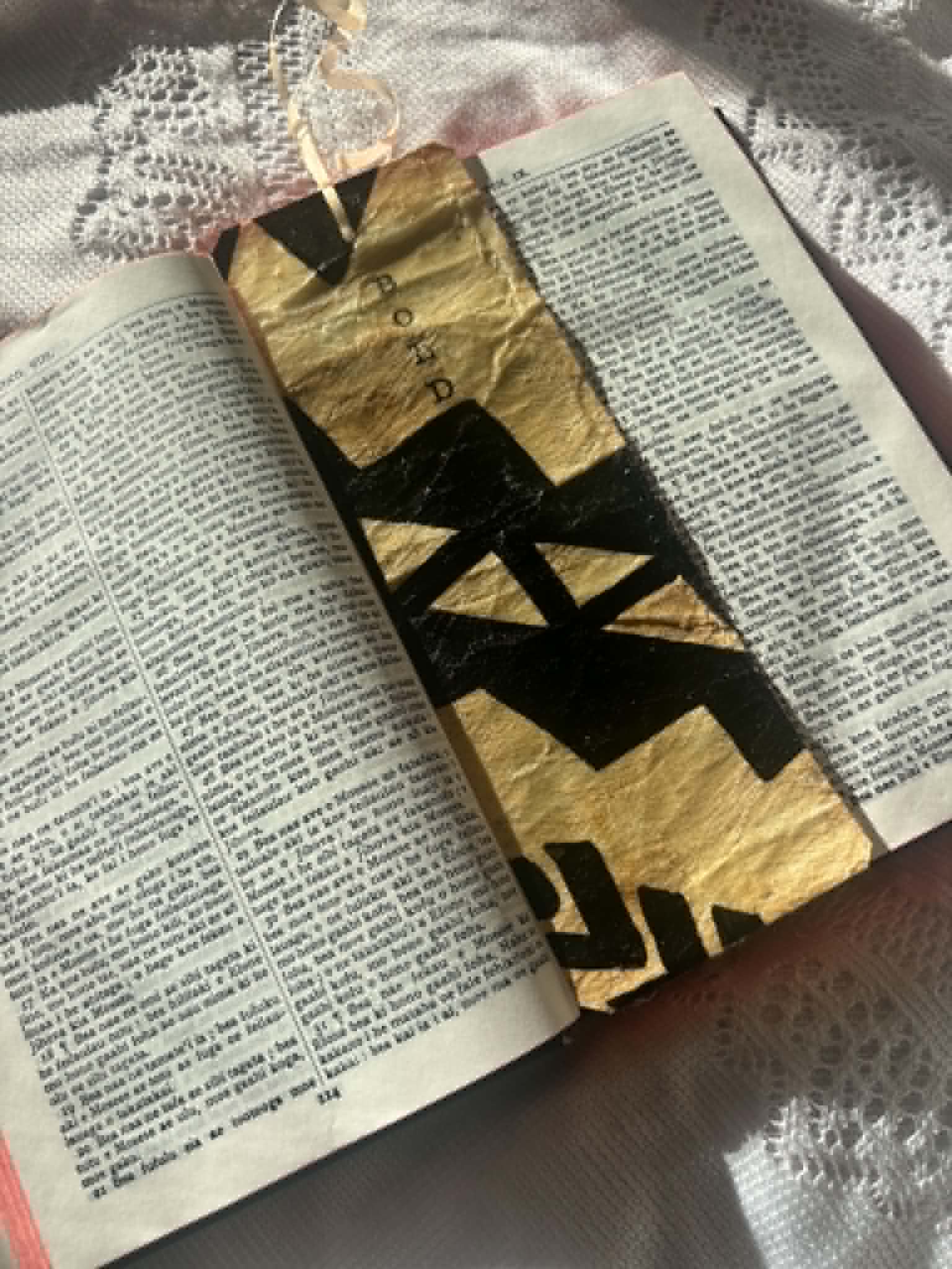 Gold fabric bookmark with bold black cross shapes and cord tie on book