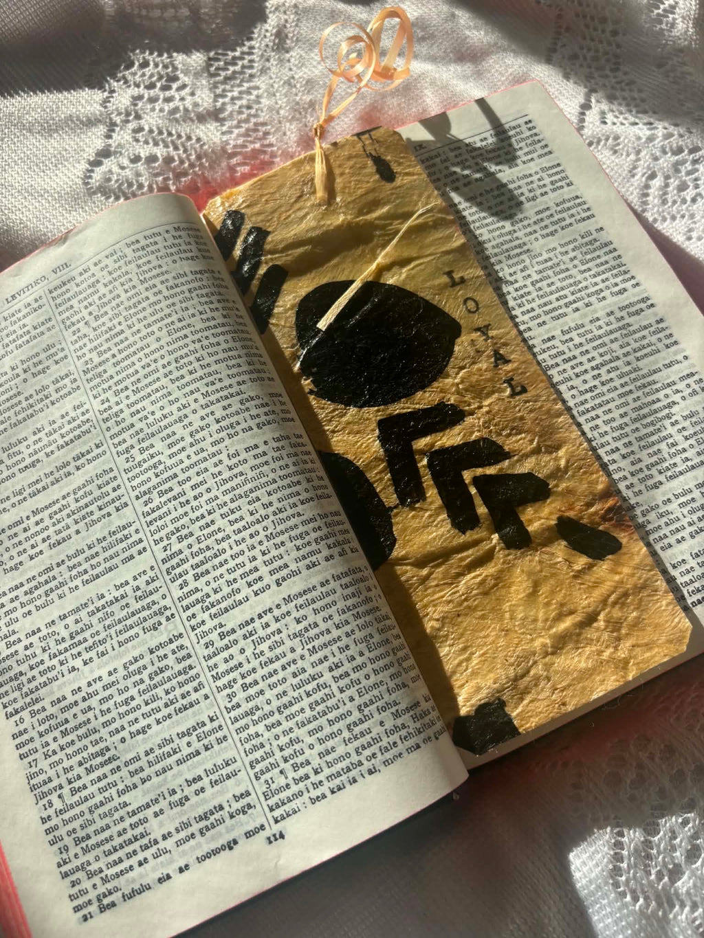 Gold foil bookmark with bold black symbols and ribbon tassel on open page