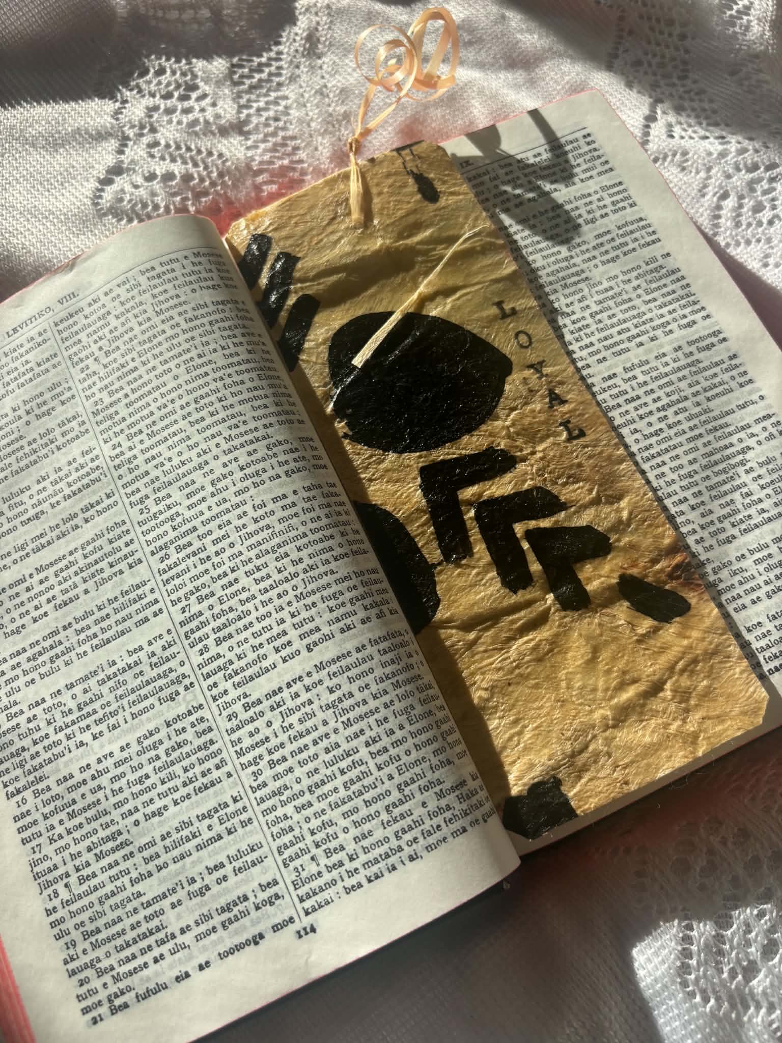Gold foil bookmark with bold black symbols and ribbon tassel on open page