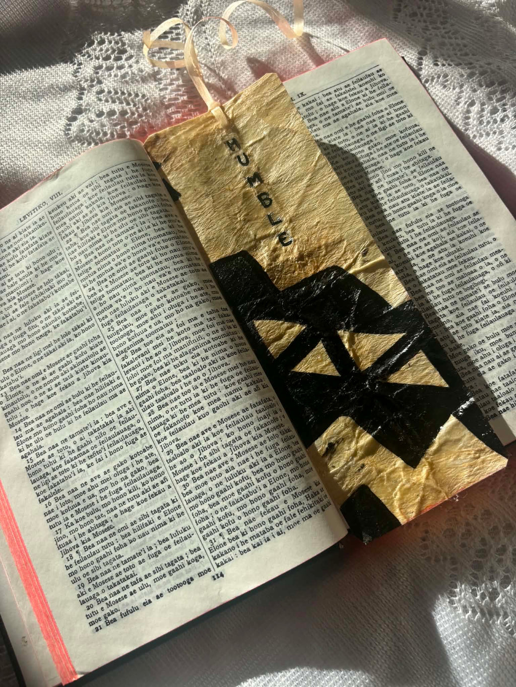 Gold foil bookmark with large black cross-like shapes and ribbon tassel on open page
