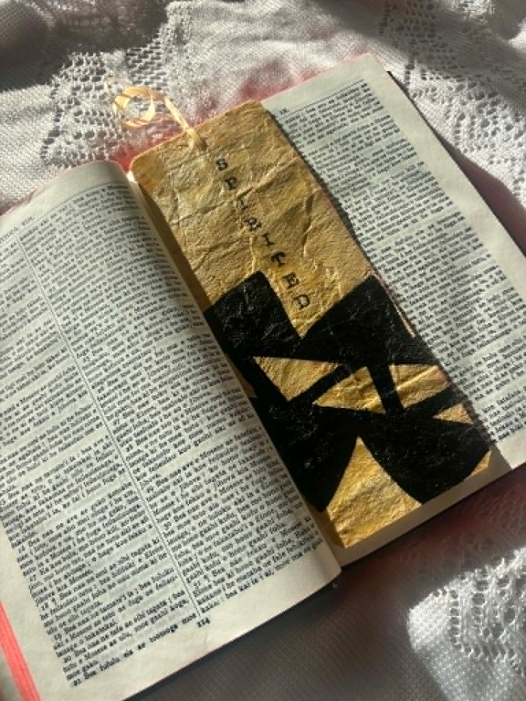 Gold fabric bookmark with black banded cross pattern and cord tie in book