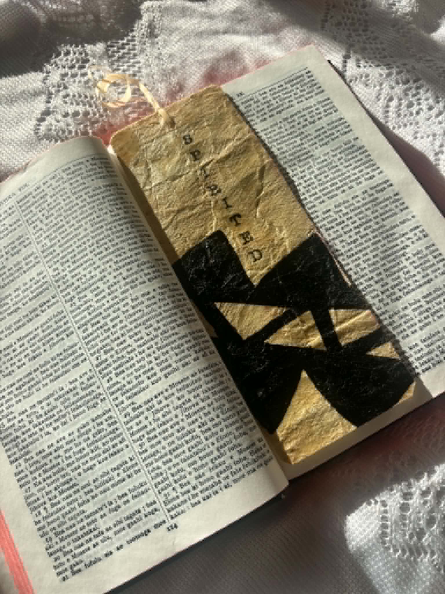 Gold fabric bookmark with black banded cross pattern and cord tie in book