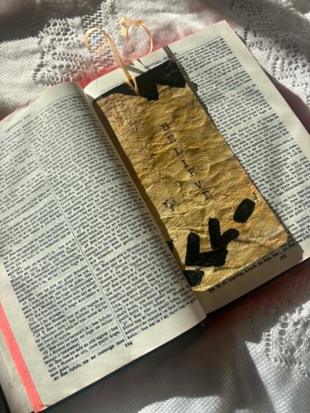 Gold fabric bookmark with black cross motif and cord tie shown on open book