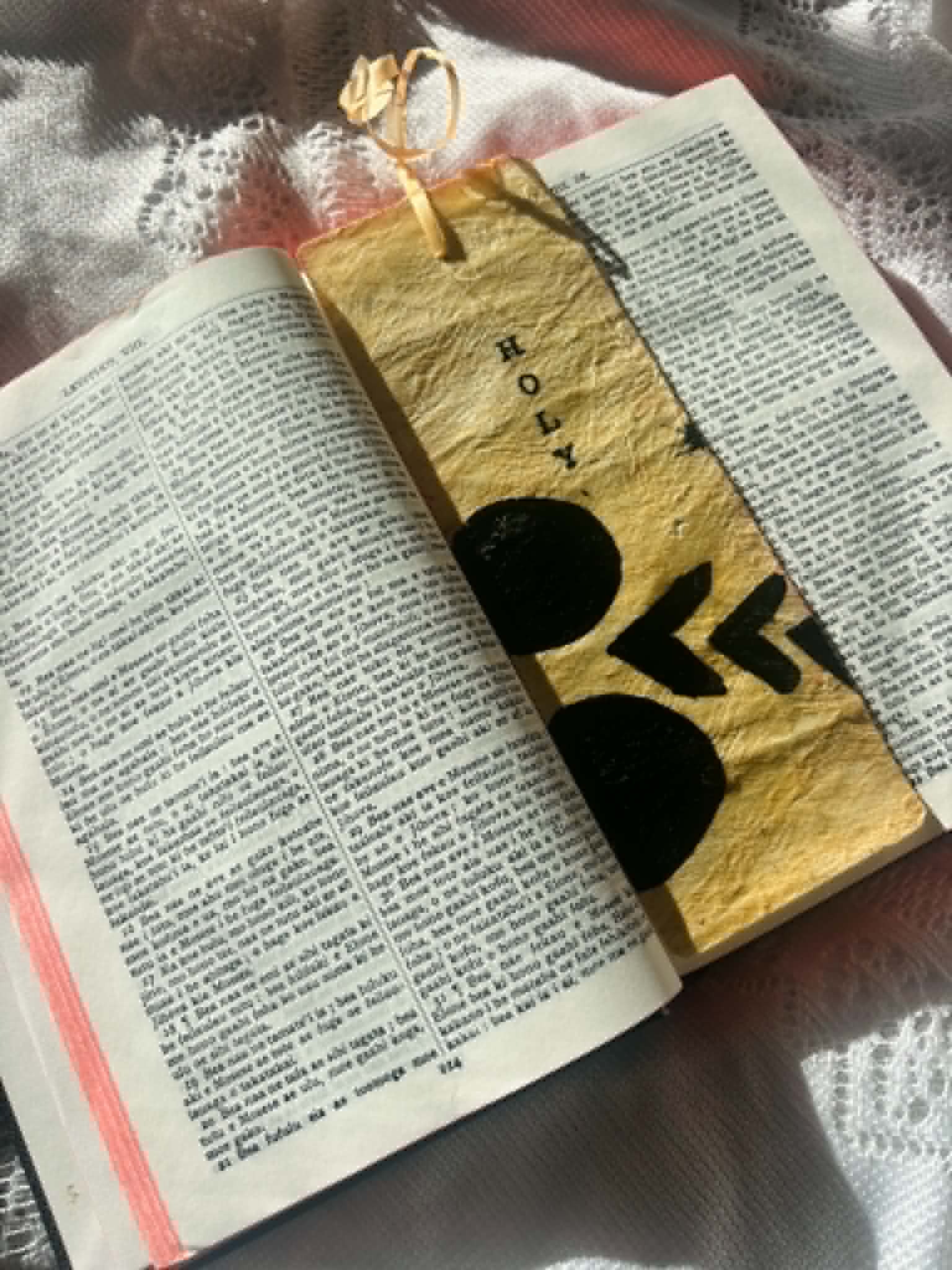 Gold fabric bookmark with black heart-like marks and cord tie on book