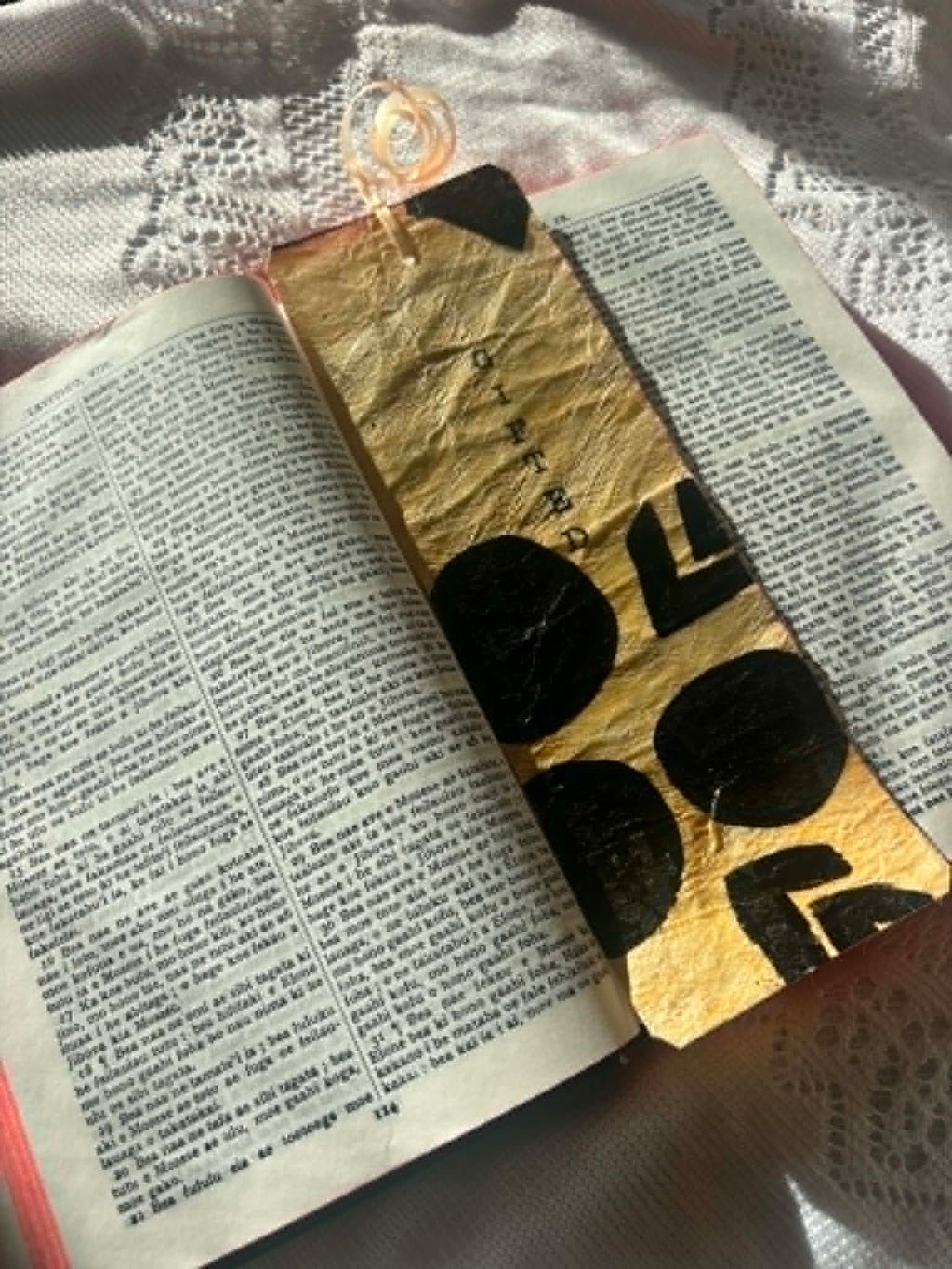 Angled gold bookmark with black letter shapes and tassel, placed between open pages