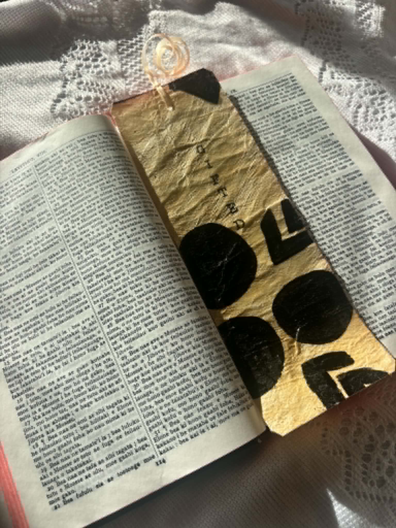 Angled gold bookmark with black letter shapes and tassel, placed between open pages