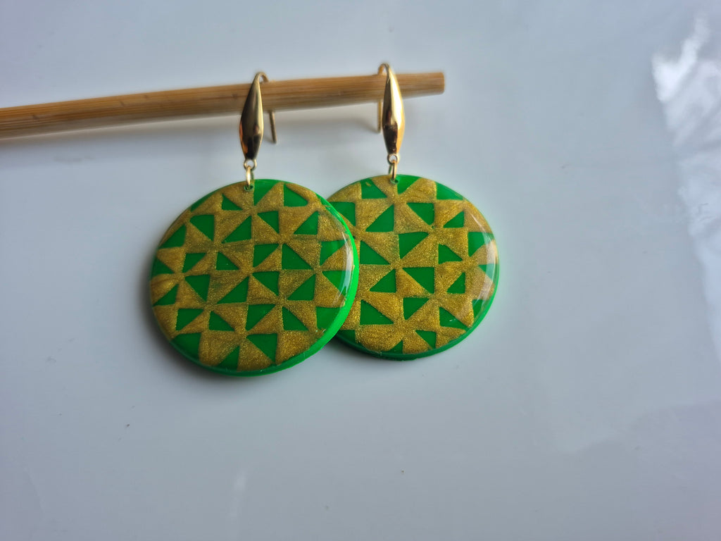 Manulua circle earrings, green circular discs with gold hooks on wooden stand.
