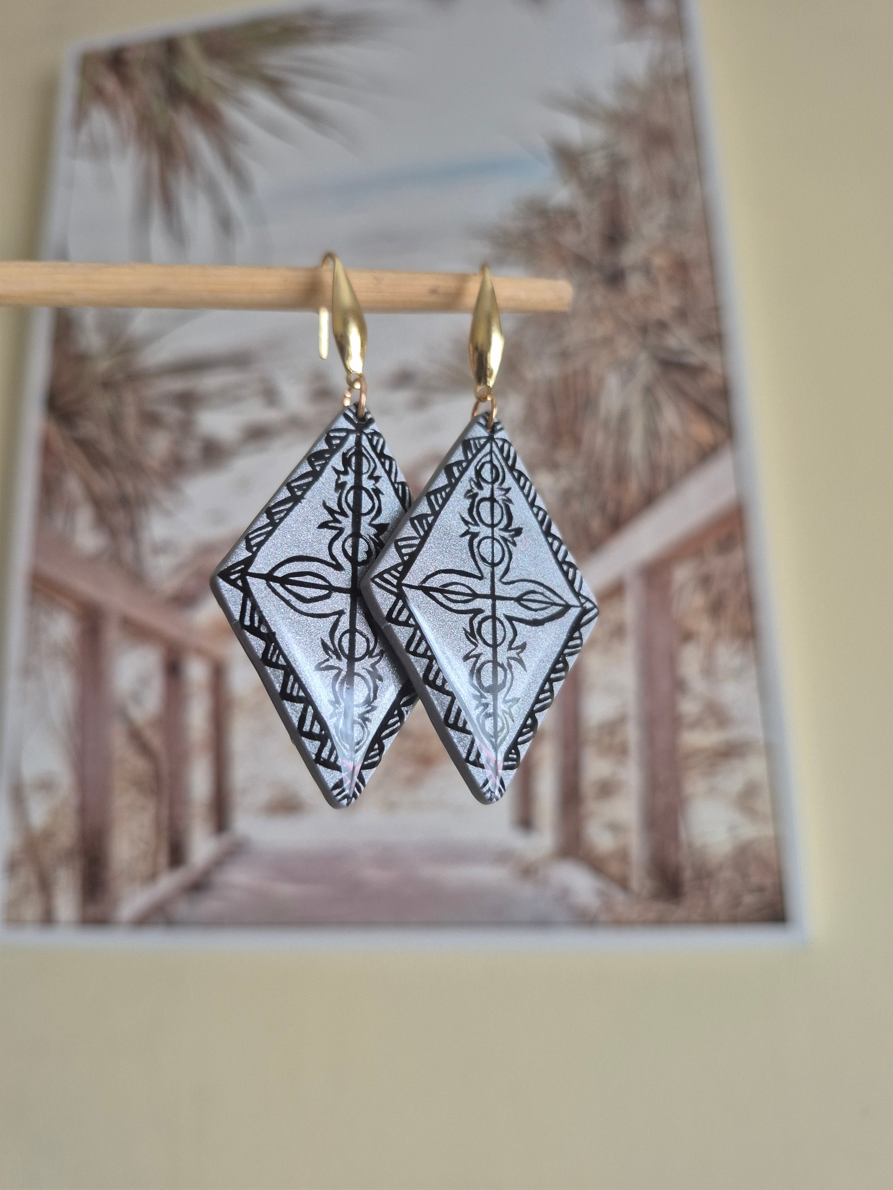 Gold hoop earrings with black-and-white patterned diamond dangles, side view